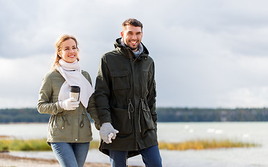 Image showing couple with tumbler walking along autumn beach