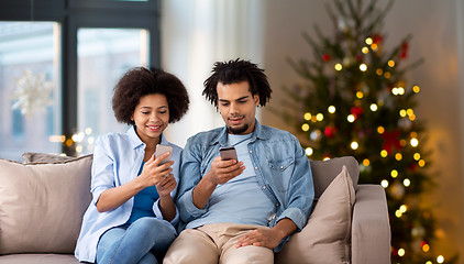 Image showing happy couple with smartphones at home on christmas