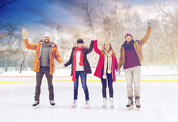 Image showing happy friends waving hands on skating rink