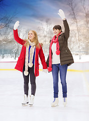 Image showing happy female friends waving hands on skating rink