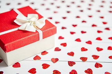Image showing Boxed gift placed on heart shaped red sequins on white wooden table