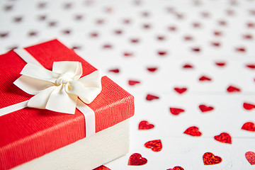 Image showing Boxed gift placed on heart shaped red sequins on white wooden table