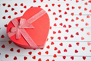 Image showing Boxed gift placed on heart shaped red sequins on white wooden table