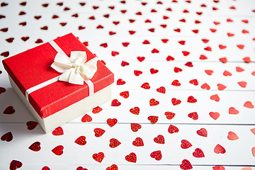 Image showing Boxed gift placed on heart shaped red sequins on white wooden table