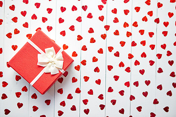 Image showing Boxed gift placed on heart shaped red sequins on white wooden table