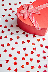 Image showing Boxed gift placed on heart shaped red sequins on white wooden table