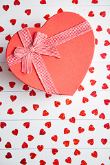 Image showing Boxed gift placed on heart shaped red sequins on white wooden table