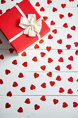 Image showing Boxed gift placed on heart shaped red sequins on white wooden table