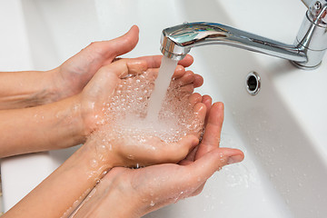 Image showing Children\'s and adult hands take water flowing from the mixer in the palm