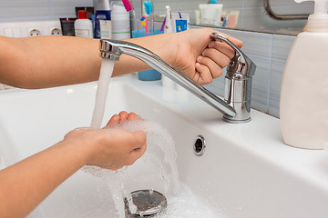 Image showing The child opens the faucet in the bathroom, and adjusts the warmth of the water