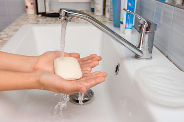 Image showing The child holds in his hands the soap on which water flows from the mixer