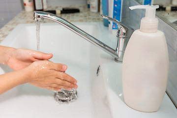 Image showing The child washes his hands under the tap, in the foreground a tube of liquid soap