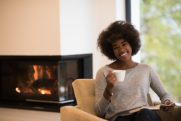 Image showing black woman reading book  in front of fireplace