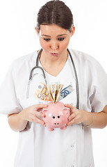 Image showing happy woman doctor with piggy bank full of money