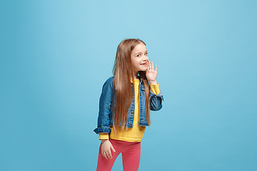 Image showing The young teen girl whispering a secret behind her hand over blue background