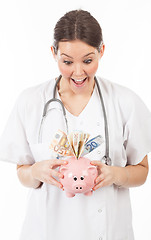 Image showing happy woman doctor with piggy bank full of money