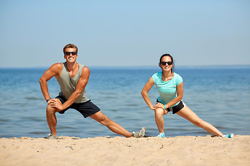 Image showing smiling couple stretching legs on beach