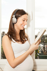 Image showing happy pregnant woman reading a book and listening to music