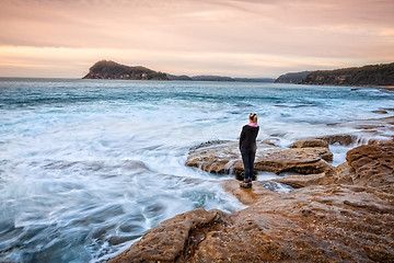 Image showing Female standing on rocks letting coastal waves wash up to her feet