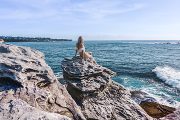 Image showing Female relaxes perched on a rock enjoying coastal views