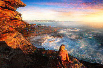 Image showing Female on rocks watching the ocean cascade around coastal rocks