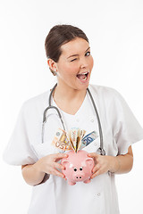 Image showing happy woman doctor with piggy bank full of money