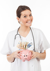 Image showing happy woman doctor with piggy bank full of money