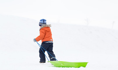 Image showing little boy with sled climbing snow hill in winter