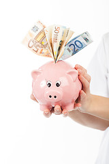 Image showing A woman shows a piggy bank full of European banknotes