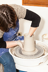 Image showing Female Potter creating a earthen jar on a Potter\'s wheel