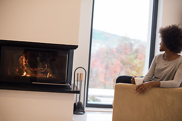 Image showing black woman drinking coffee in front of fireplace