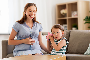 Image showing pregnant mother and daughter with piggy bank