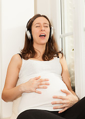 Image showing happy pregnant woman singing and listening to music