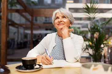 Image showing senior woman with notebook dreaming at street cafe