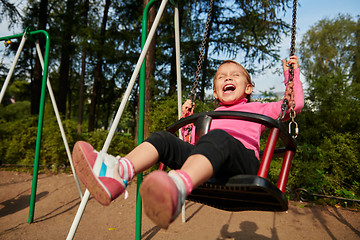 Image showing Little girl with funny facial expression swinging on the swings