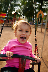 Image showing Little girl with funny facial expression swinging on the swings