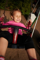 Image showing Little girl with funny facial expression swinging on the swings