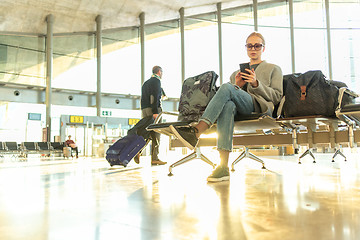 Image showing Female traveler using her cell phone while waiting to board a plane at departure gates at airport terminal.