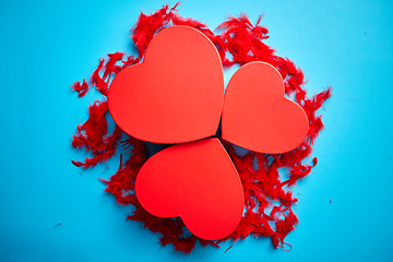 Image showing Three red, heart shaped gift boxes placed on blue background among red feathers