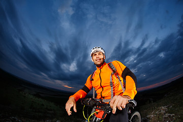 Image showing cyclist standing with mountain bike on trail at sunset