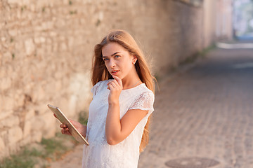 Image showing beautiful young woman in white dress using tablet