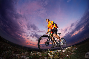 Image showing cyclist standing with mountain bike on trail at sunset