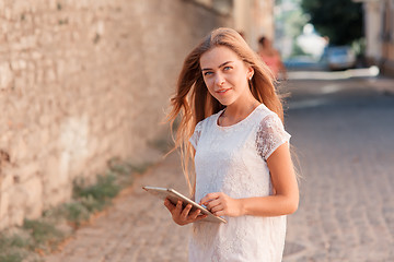 Image showing beautiful young woman in white dress using tablet