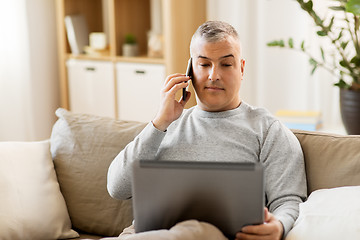 Image showing man with laptop calling on smartphone at home