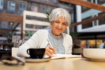 Image showing senior woman writing to notebook at street cafe