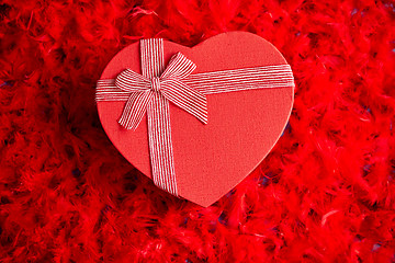 Image showing Heart shaped boxed gift, placed on red feathers background