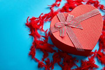 Image showing Red, heart shaped gift box placed on blue background among red f