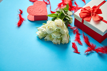 Image showing Bouquet of white roses with red bow on blue background. Boxed gift on side