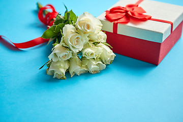 Image showing Bouquet of white roses with red bow on blue background. Boxed gift on side