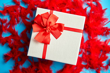 Image showing Box with a gift, tied with a ribbon placed on red feathers